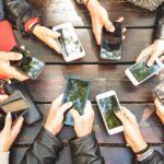 Grupo de pessoas sentadas em uma mesa usando smartphones, representando o uso excessivo de telas no cotidiano