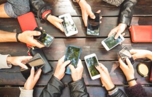 Grupo de pessoas sentadas em uma mesa usando smartphones, representando o uso excessivo de telas no cotidiano