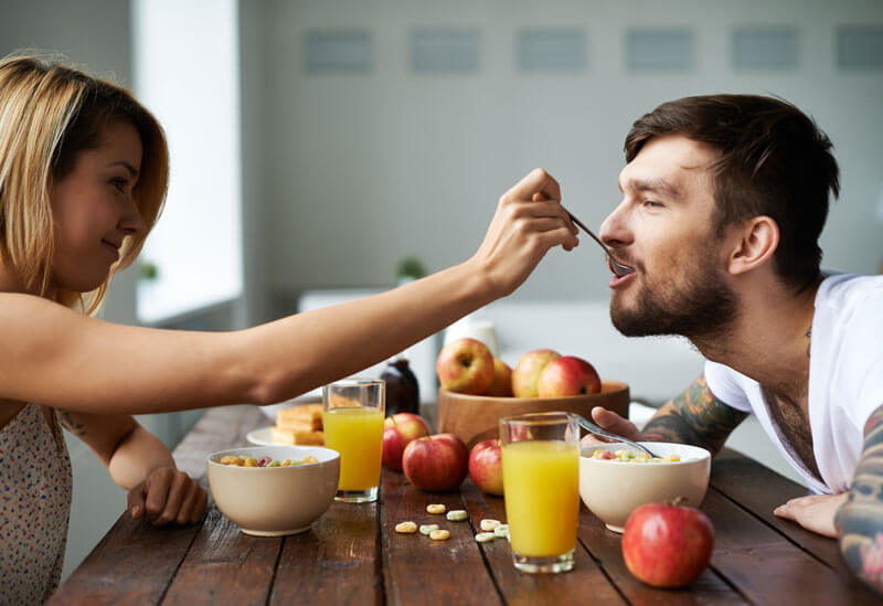Casal tomando café da manhã saudável com frutas, pães integrais e café, representando os benefícios de começar o dia com uma refeição equilibrada