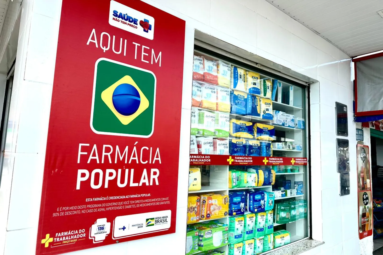 Entrada de farmácia exibindo o adesivo “Aqui tem Farmácia Popular”
