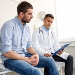 Homem de cerca de 30 anos em consulta médica realizando check-up de rotina, representando a importância de exames preventivos para a saúde masculina