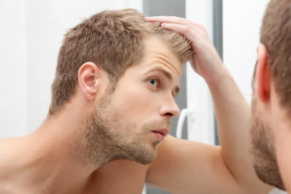 Homem preocupado observando a queda de cabelo masculina no espelho