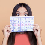 Mulher segura calendário com ciclo menstrual marcado, representando atenção à saúde feminina e regularidade da menstruação
