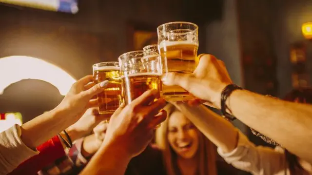 Grupo de amigos brindando com copos de cerveja durante encontro social noturno