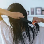 Pessoa penteando o cabelo úmido em casa, ilustrando o hábito de secar o cabelo antes de dormir