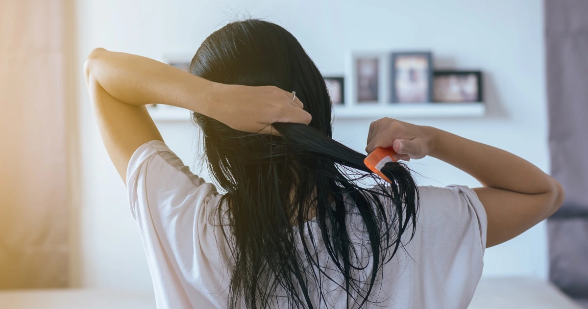 Pessoa penteando o cabelo úmido em casa, ilustrando o hábito de secar o cabelo antes de dormir